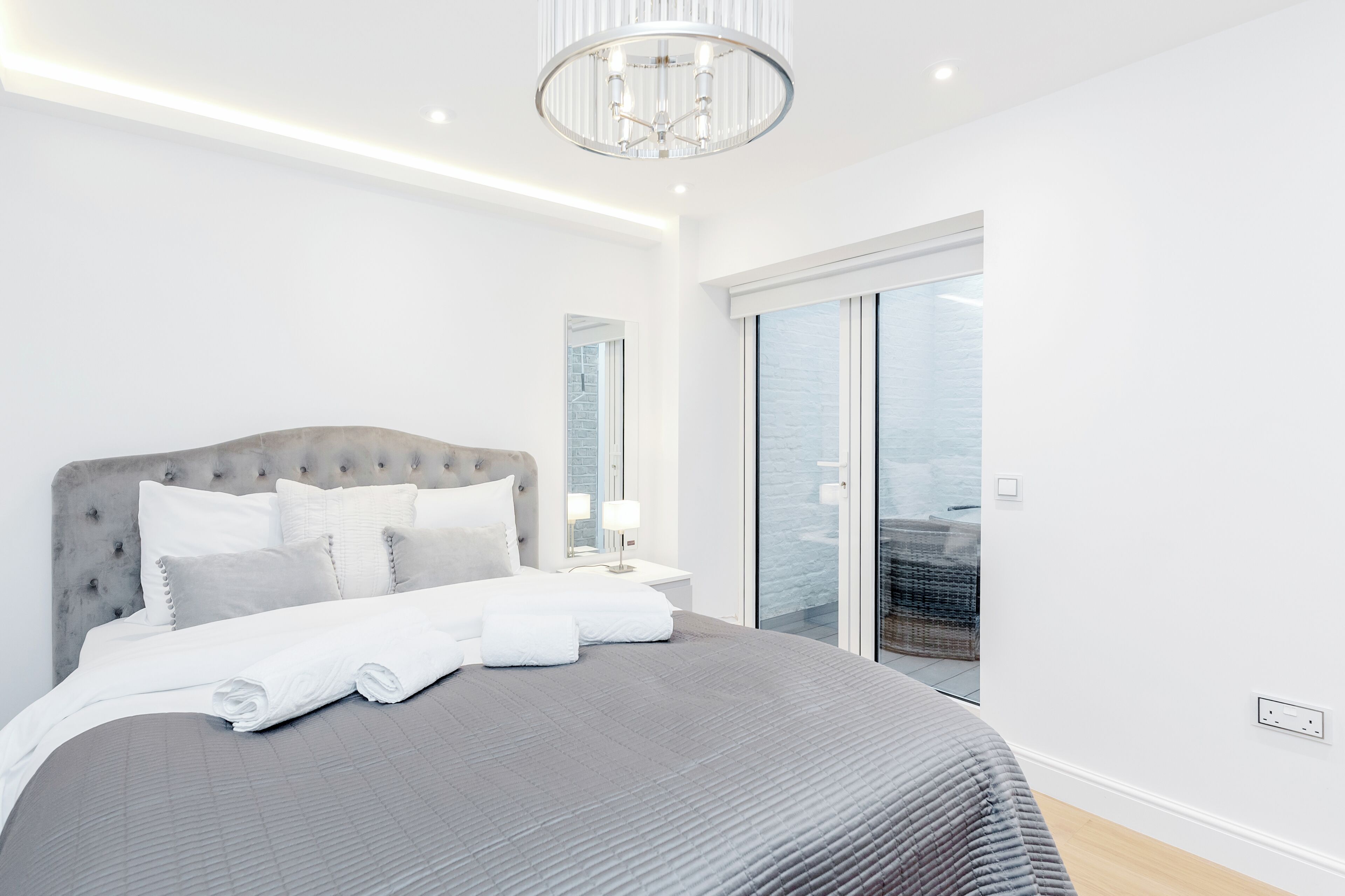 Une chambre moderne avec un grand lit, un lustre et une vue sur l’extérieur.