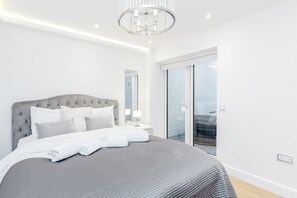 A modern bedroom with a large bed, a chandelier, and a view of the outdoors.
