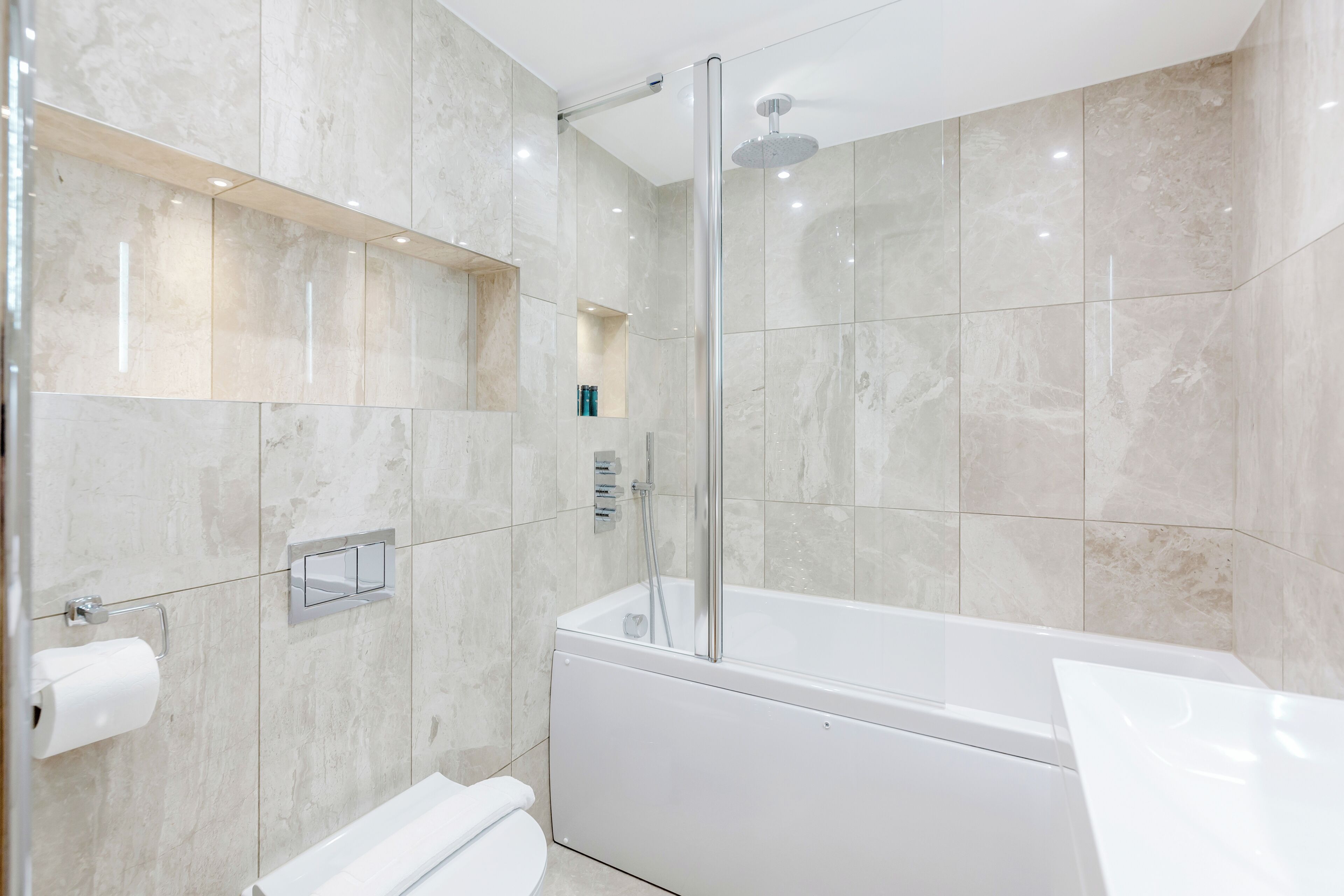 A modern bathroom with a glass-enclosed shower, a white bathtub, and a built-in toilet.