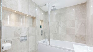 Moderni kylpyhuone, jossa on lasiseinällä varustettu suihku, valkoinen kylpyamme ja seinään upotettu wc-istuin.
