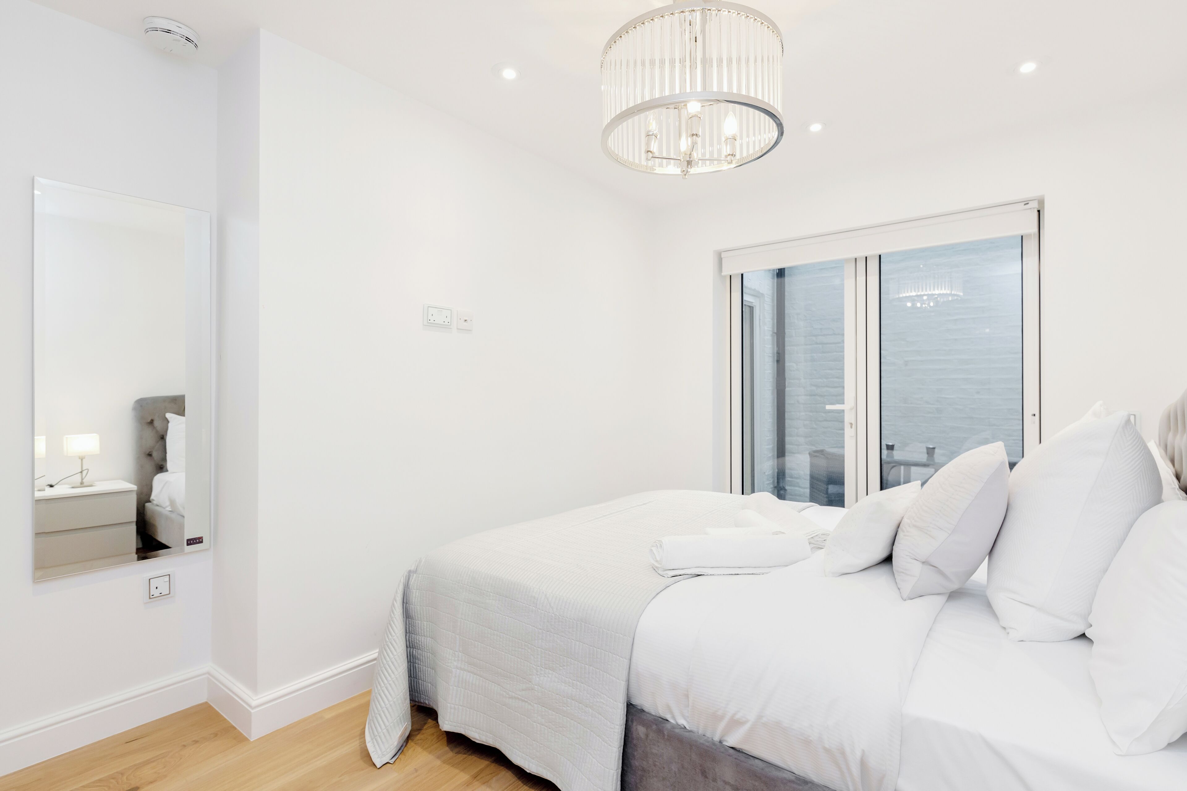 Une chambre moderne avec un grand lit, une table de chevet, un miroir et un lustre.