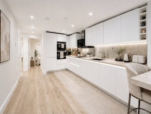 A modern kitchen with white cabinetry, a central island, a built-in oven, and a microwave. - Luxury Knightsbridge Apt by Harrods. Full A/C (London)