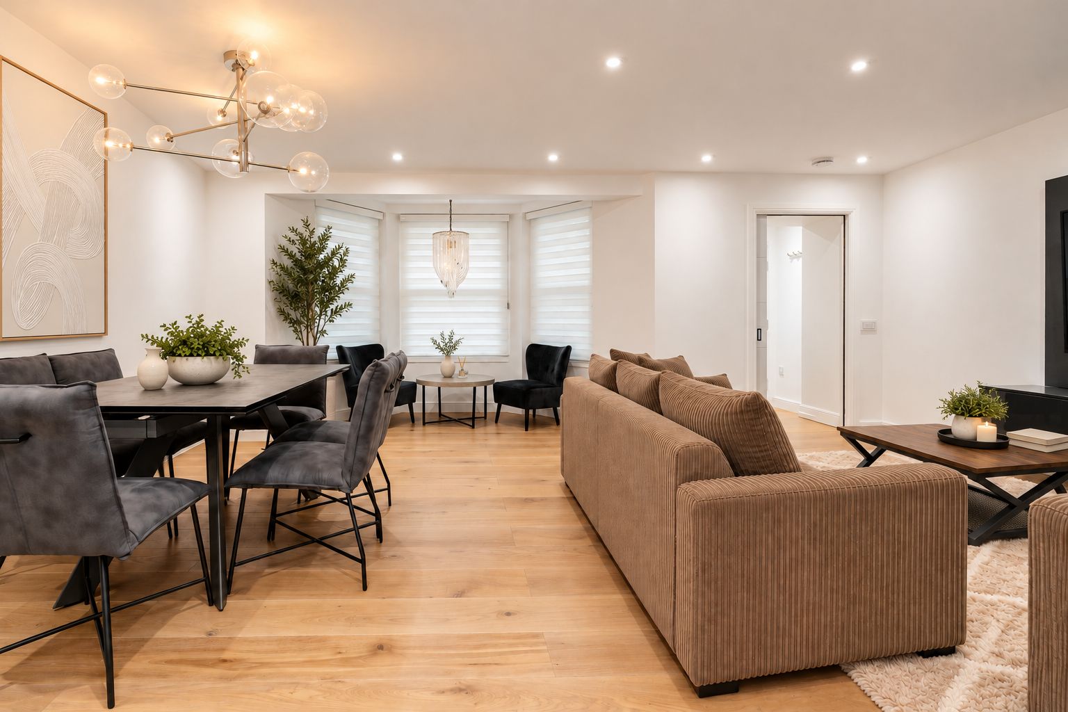 Un salon moderne avec un coin repas, comprenant un ensemble de canapés, une table à manger avec des chaises, un lustre et une plante en pot.