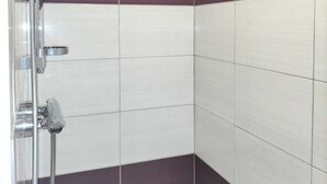 Un espace douche doté d’un pommeau et d’une poignée de douche en chrome, de murs carrelés avec un motif rayé alternant le blanc et le marron foncé, et d’une conception d’angle.