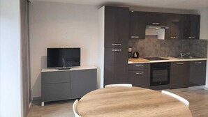 Une cuisine moderne avec des meubles de rangement aux couleurs sombres, une table à manger en bois et un téléviseur à écran plat posé sur un meuble.