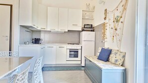 A compact kitchen with white cabinets, a built-in oven, and a small dining area with a table and chairs. - [Cedro] Apartment with swimming pool (Orosei)