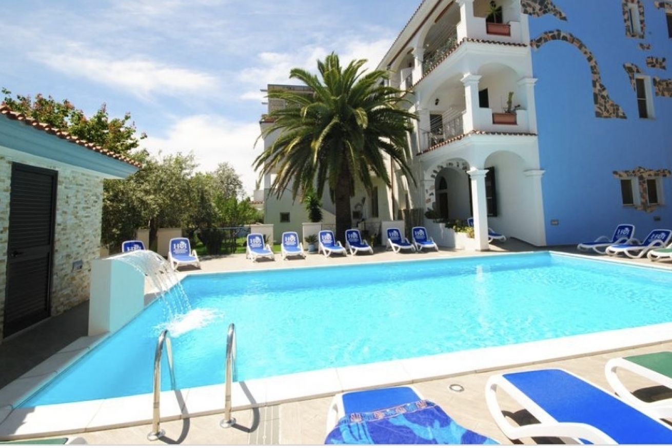 Ein Swimmingpool mit Liegestühlen, einer Palme und einem Gebäude mit Balkonen.