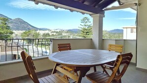 A round wooden table with four chairs on a balcony with a metal railing, overlooking a mountainous landscape. - [Cedro] Apartment with swimming pool (Orosei)