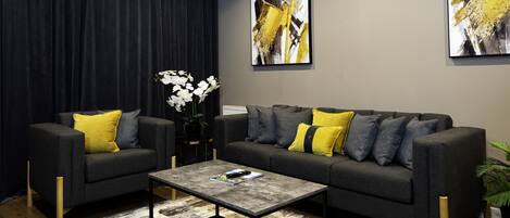 A modern living room with a grey sofa set, yellow and grey cushions, a coffee table, and a large window with dark curtains.