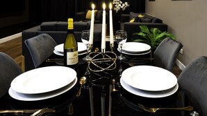 A dining table set with white plates, gold cutlery, a bottle of wine, and three lit candles.