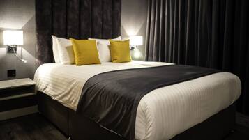 A modern hotel room with a large bed, two bedside lamps, and a dark curtain backdrop.