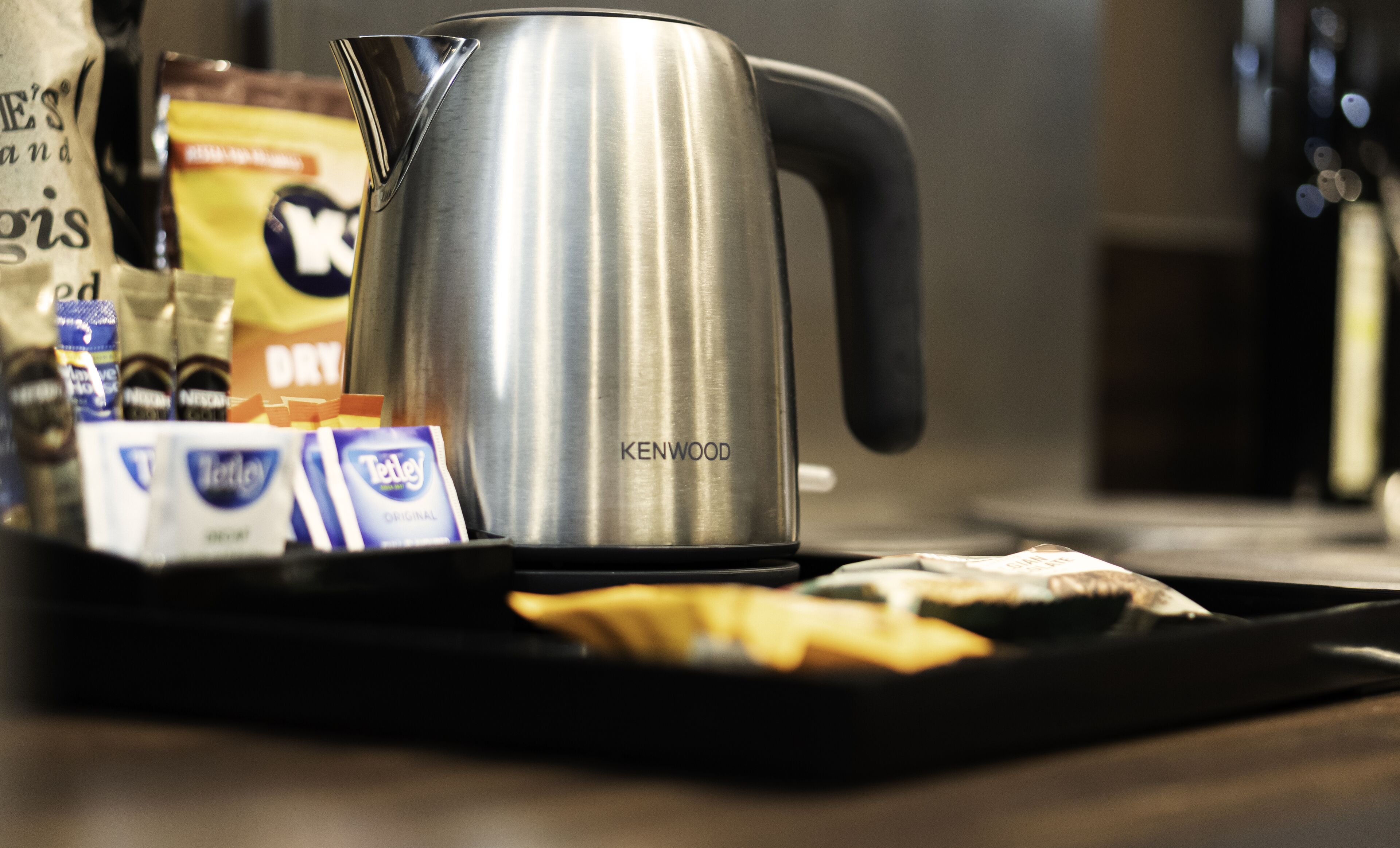 Una moka Kenwood in acciaio inossidabile su un vassoio con diverse cialde per caffè e un pacchetto di zucchero.
