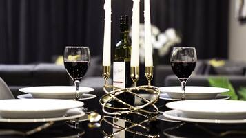 A dining table set with white plates, two wine glasses, a bottle of wine, and four lit candles.