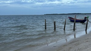 A beach with a boat moored near the shore, wooden posts, and a distant shoreline. - Pousada Essência de Atins (Barreirinhas)