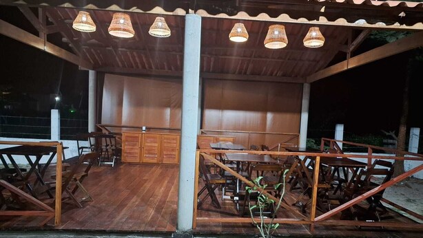 An outdoor dining area with wooden tables and chairs, a central bar, and hanging lights. - Pousada Essência de Atins (Barreirinhas)