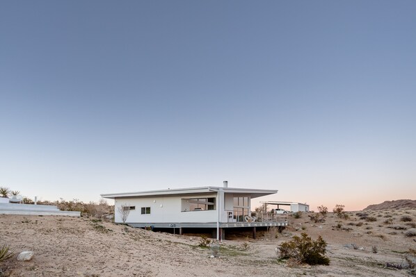 A modern, single-story house with a flat roof, large windows, and a covered outdoor area.