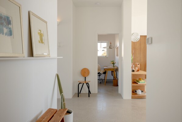 A hallway with a wooden bench, a chair, and a potted plant. There are framed pictures on the wall and a wooden shelf with decorative items. - Panorama House: Featured in Dwell (Yucca Valley)