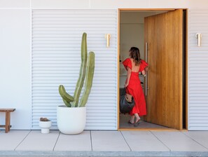 A woman in a red dress exiting a building with a large cactus plant outside. - Panorama House: Featured in Dwell (Yucca Valley)