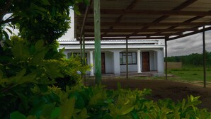 A covered outdoor area with a white building, columns, and a wooden roof. - Asphumule Lodge (Siphofaneni)