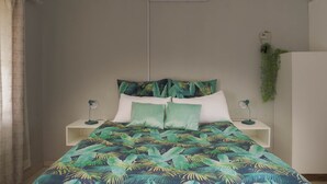 A bedroom with a bed, two nightstands, a wall-mounted air conditioner, and a small plant. - Asphumule Lodge (Siphofaneni)