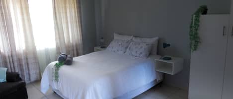 Un dormitorio con cama, mesitas de noche, cómoda y ventana con cortinas.