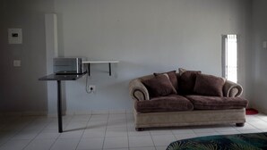 A living room with a beige sofa, a small table, and a white wall. - Asphumule Lodge (Siphofaneni)