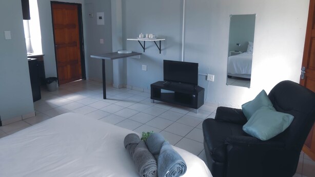 A hotel room with a bed, a TV, a chair, a small table, and a mirror. - Asphumule Lodge (Siphofaneni)