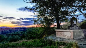Estructura de piedra con un pequeño refugio, rodeada de vegetación exuberante y vista a un valle al atardecer.