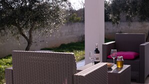 Des meubles en osier, une bouteille de vin et un verre, un bocal avec un couvercle, et un coussin rose sur une table.