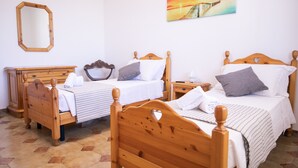 Une chambre à coucher avec deux lits en bois, une commode en bois, un miroir et un tableau accroché au mur.