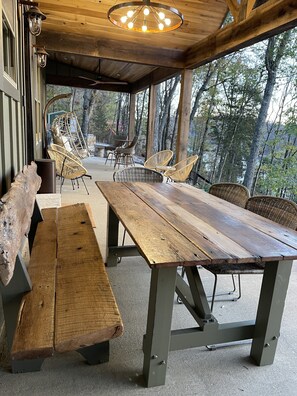 A wooden dining table with benches, surrounded by wicker chairs, under a wooden ceiling with a hanging light fixture. - Sunset Lake Cottage at Mammoth Cave (Mammoth Cave)