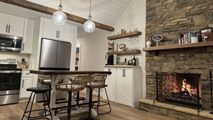 A modern kitchen with white cabinets, stainless steel appliances, and a stone fireplace. - Sunset Lake Cottage at Mammoth Cave (Mammoth Cave)