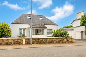 Une maison à deux étages, avec des fondations en pierre, un toit à deux versants et une porte de garage visible.