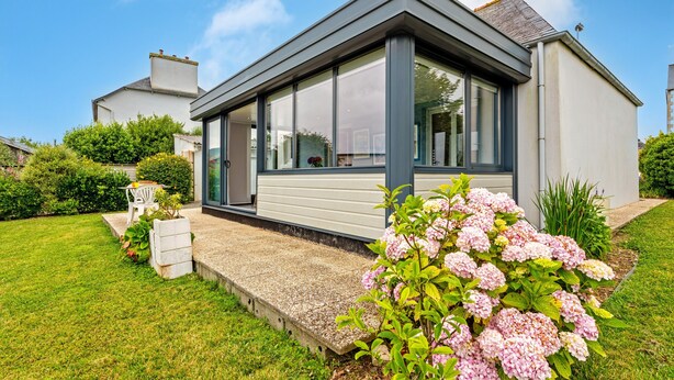 Une maison moderne dotée d’une grande fenêtre, d’une pelouse bien entretenue et d’un parterre de fleurs.