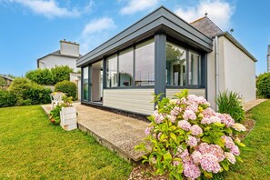 Une maison moderne dotée d’une grande fenêtre, d’une pelouse bien entretenue et d’un parterre de fleurs.