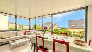 Un espace de repas lumineux, avec une table dressée pour deux personnes, un canapé et de grandes fenêtres donnant sur le quartier.