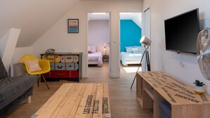 A modern room with a sofa, a wooden coffee table, a TV, and a bed with a blue wall.