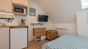 Una kitchenette compacta con microondas, un refrigerador pequeño, un escritorio de madera, un televisor y una cama con cubrecama estampado.