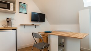 Una kitchenette compacta con microondas, cafetera y televisor montado en la pared.