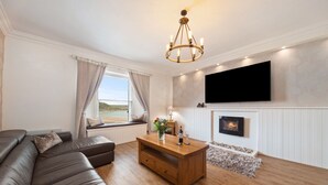 A modern living room with a sectional sofa, a wooden coffee table, a fireplace, and a mounted TV. - Stunning Seafront Apartment in the heart of Tenby (Tenby)