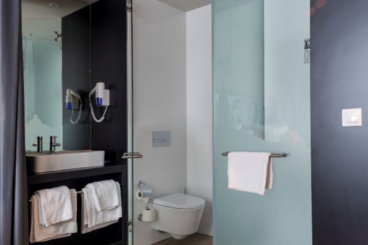 Un baño moderno con una pared oscura, cabina de ducha de vidrio, inodoro blanco y lavabo con dos toallas.