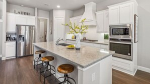 A modern kitchen with white cabinetry, stainless steel appliances, a granite countertop, and a central island with stools.