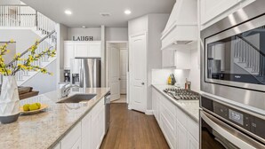 A modern kitchen with white cabinetry, stainless steel appliances, and a marble countertop.