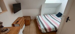 Un dormitorio con cama, escritorio, televisor y ventana.