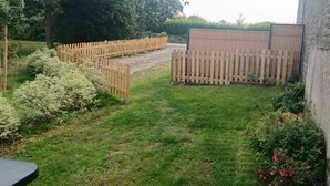 Un jardín con cerca de madera, muro de concreto y plantas con flores.