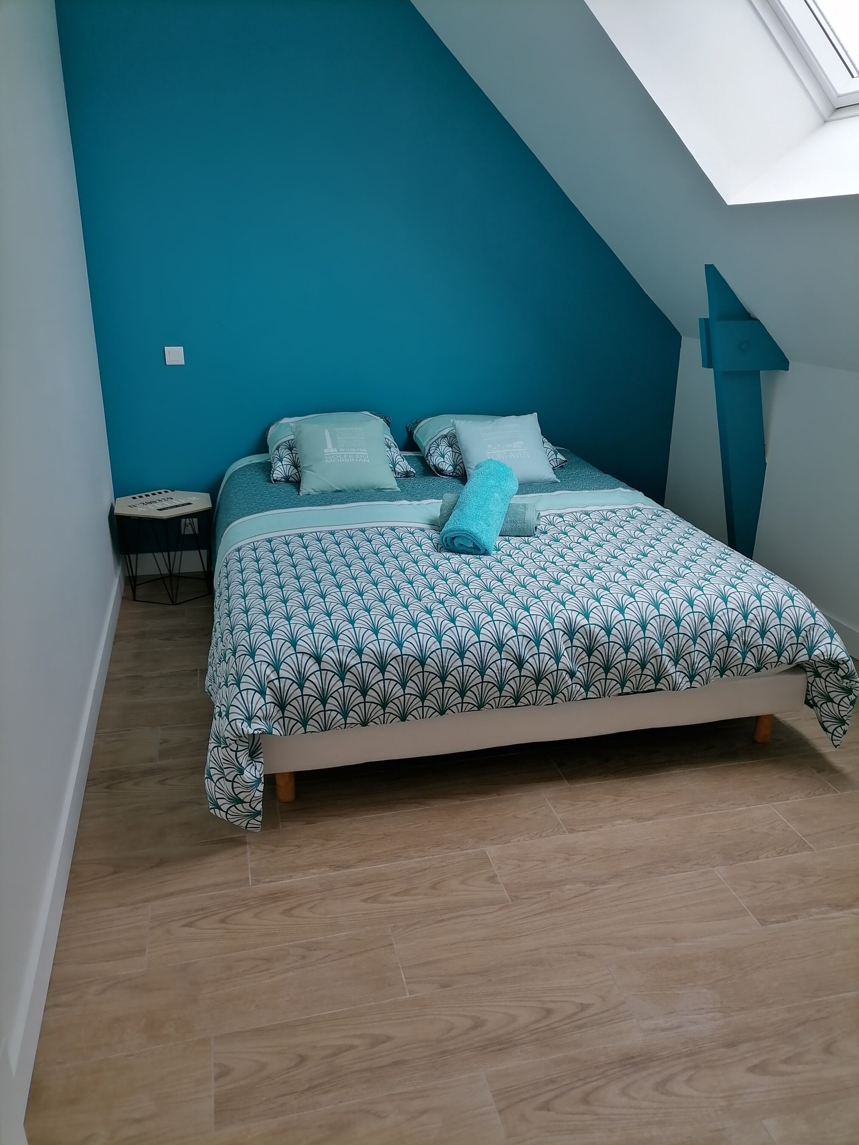 Un dormitorio con cama, almohadas, una mesita y un estante en la pared.