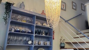 Een trap met een blauwe leuning, een blauwe plank met verschillende glazen en decoratieve objecten, en een hangende lamp.