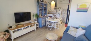 Ein Wohnzimmer mit Fernseher, Esstisch, Stühlen, einem blauen Sofa und einer Treppe.