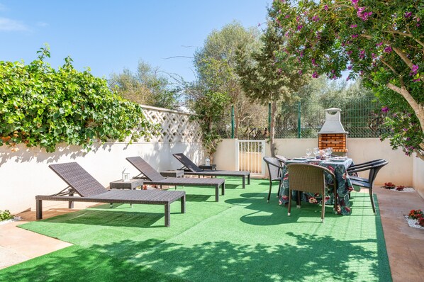 Un patio exterior con sillones, una mesa lista para comer y un horno de ladrillo.