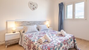 Un dormitorio con cama, mesitas de noche, una decoración de corazón en la pared y una ventana con cortinas.